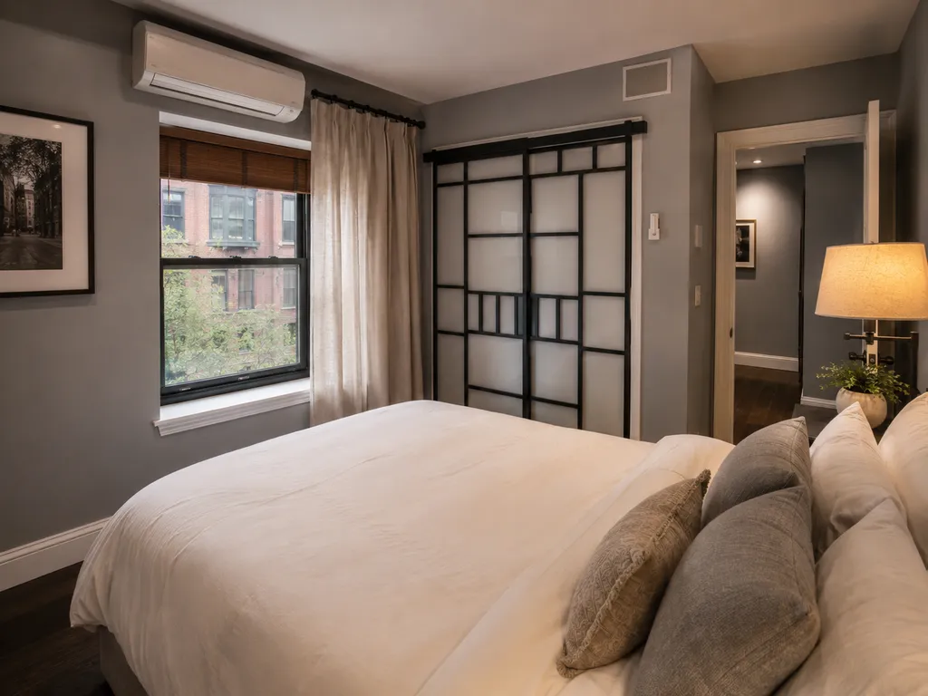 A bedroom with a bed, pillows, a lamp, and a window with a view outside.