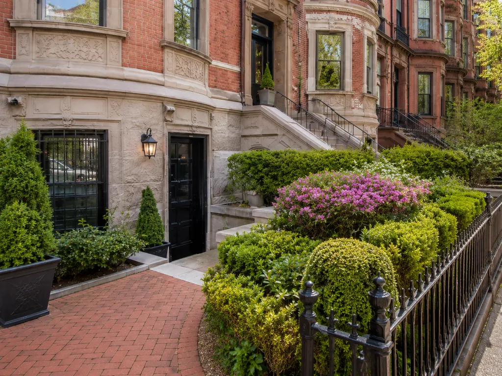 Brick building with black door, hedges, and a brick walkway.